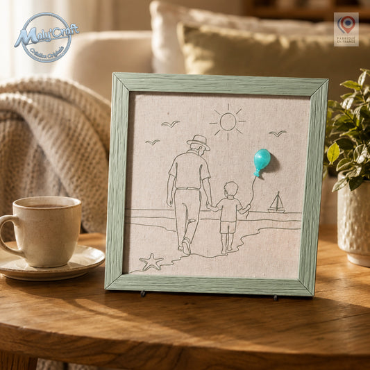 Peut inclure: Une décoration murale carrée encadrée présentant un dessin au trait noir sur un fond en tissu beige clair. L'illustration représente un adulte et un enfant marchant sur une plage, avec un petit ballon turquoise en relief sur la main.