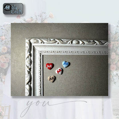 Lot de petits cœurs personnalisés en 3D avec initiales, posés sur un fond textile beige encadré, parfaits comme cadeaux d'invités de mariage.