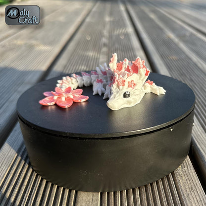 Dragon articulé Sakura blanc et rose, création Cinderwing3D, imprimé en 3D par Maly’Craft. Figurine flexible inspirée des fleurs de cerisier, présentée dans différents décors naturels et sur fond uni. Idéale pour la décoration, la collection ou un cadeau poétique aux tons printaniers.