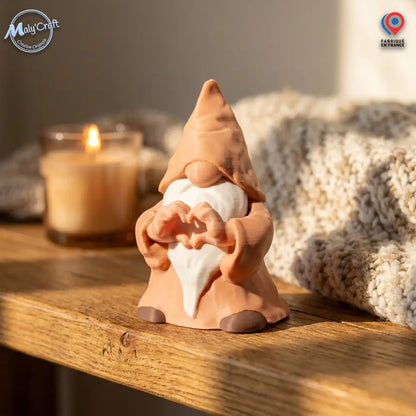 MalyCraft : gnome Figurine originale imprimée en 3D en France. Geste cœur précis, barbe blanche et robe terra cotta. Texture technique visible sous lumière Golden Hour sur étagère bois. Ambiance bougie et plaid. Précision MalyCraft.
 MalyCraft: Original 3D printed gnome figurine made in France. Precise heart hands gesture, white beard, terra cotta robes. Subtle precision 3D texture in warm Golden Hour light. Wood shelf, candle, blanket bokeh. Precision Mal