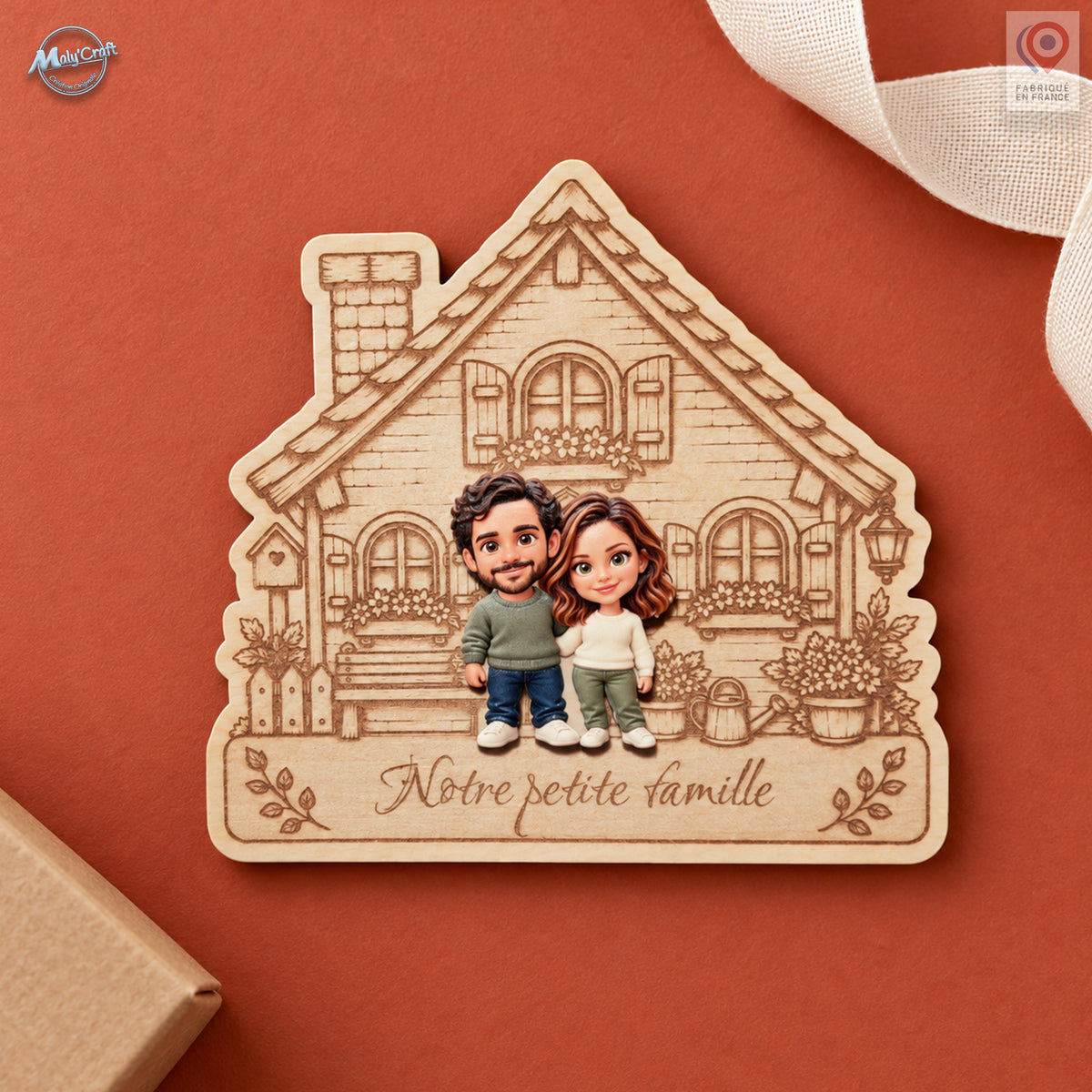 Portrait de couple personnalisé sur une maison en bois clair gravé, présenté sur un fond terracotta. Les deux personnages portent des vêtements verts, crème et bleus. L’inscription Notre petite famille apparaît sous le couple ; un ruban écru et un coin d’emballage kraft complètent la composition.
Personalized couple portrait on an engraved light-wood house plaque, displayed on a terracotta background. The chibi figures wear green, cream and blue clothing above the French inscription Notre petite famille. A 