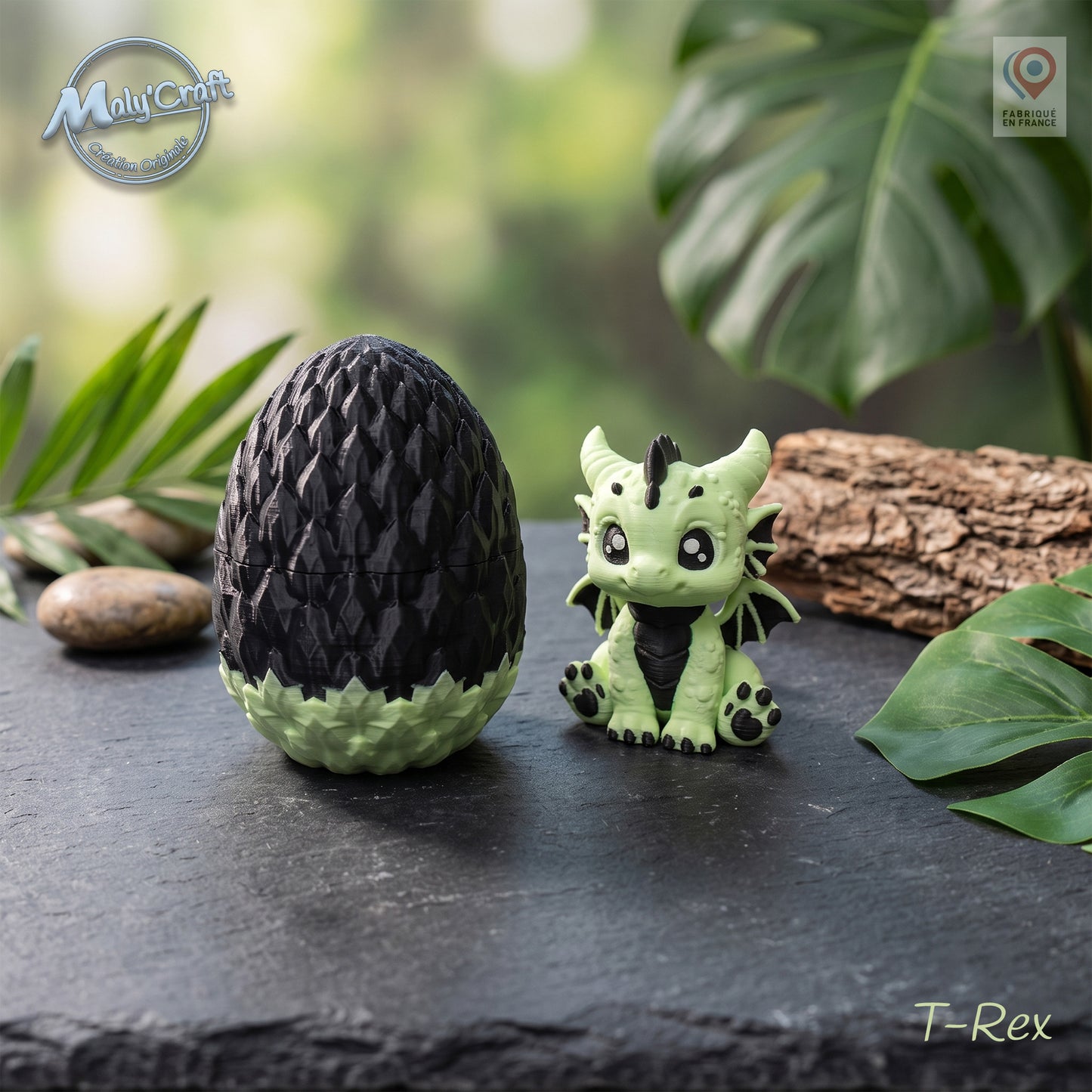 Figurine bébé dragon T-Rex vert eucalyptus et noir avec son œuf bicolore noir et vert, posés sur une surface en ardoise. Création originale MalyCraft3D, impression 3D de précision réalisée en France. Dragon kawaii multicolore avec détails écailles. Ambiance nature avec feuilles tropicales, galets et bois brut en arrière-plan.