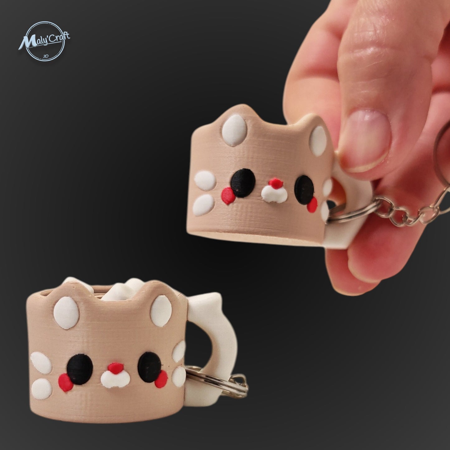 Porte-clés original en forme de petite tasse de café stylisée en tête de chat beige. L'objet présente des détails soignés : de petites oreilles pointues, des joues blanches, des yeux noirs et un petit nez rouge. Une main tient le porte-clés pour montrer sa taille compacte sur un fond noir élégant. Il s'agit d'une impression 3D de précision réalisée avec une finition mate.