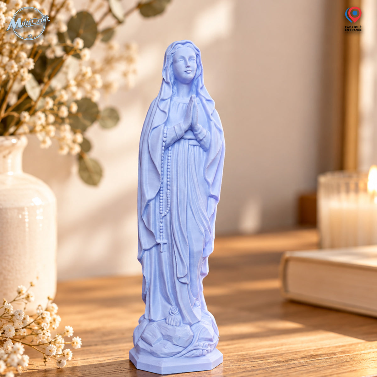 Statuette Vierge Marie bleu pastel imprimée en 3D, figurine religieuse décorative avec mains jointes, chapelet et robe sculptée, présentée sur une console en bois clair dans un intérieur chaleureux avec fleurs séchées et bougie en arrière-plan.
Pastel blue Virgin Mary statue, 3D printed religious decorative figurine with praying hands, rosary and sculpted robe, displayed on a light wood console in a warm interior with dried flowers and a candle in the background.